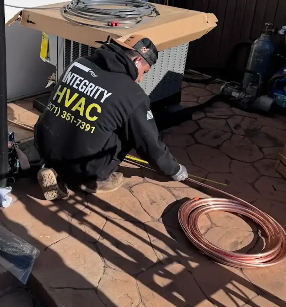 HVAC technician installing copper refrigerant line set for outdoor unit