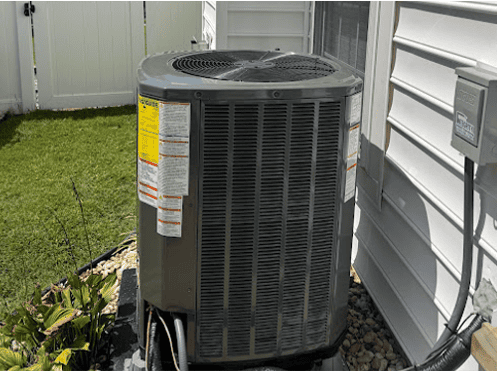 Residential outdoor air conditioning condenser installed beside a home with electrical disconnect and accessible equipment placement